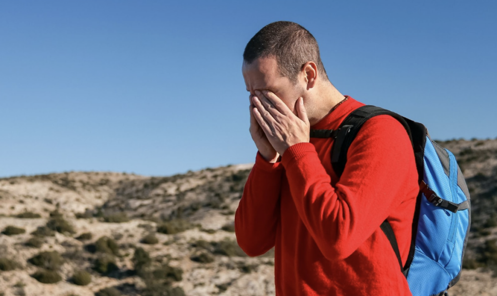 Male hiking with migraine holding head
